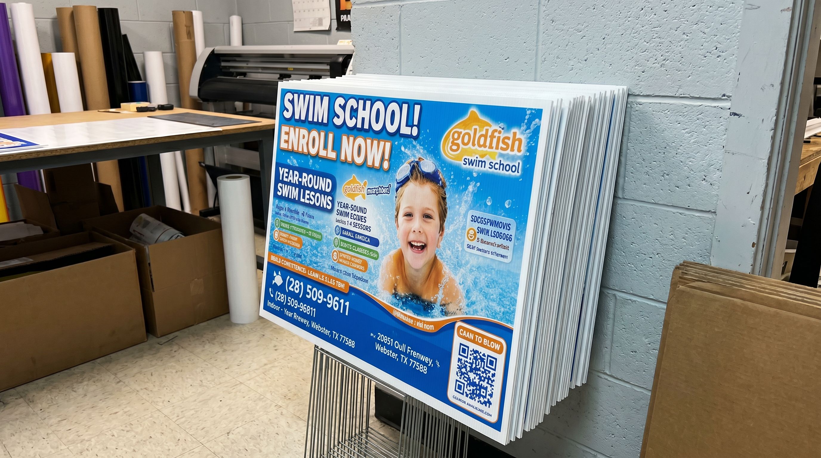 Freshly printed swim school coroplast signs stacked in the shop